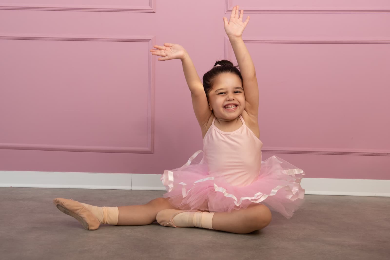 Smiling little dancer stretching against a pink wall