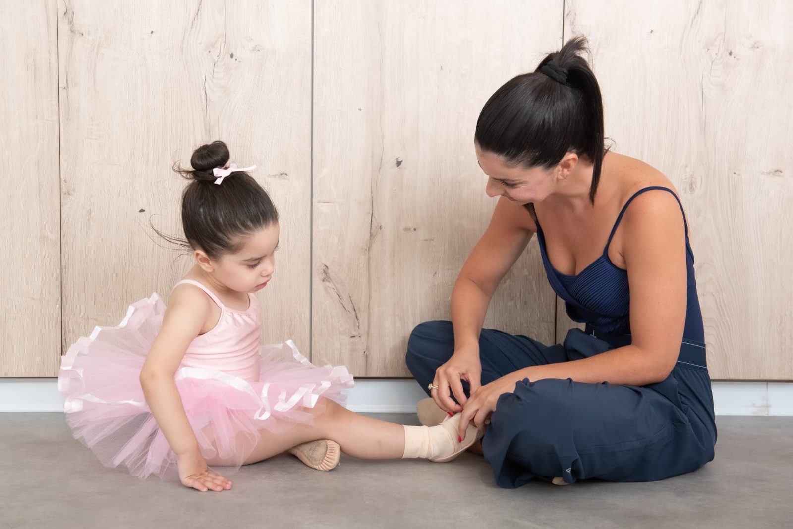 Teacher helping a young ballerina with her ballet shoes